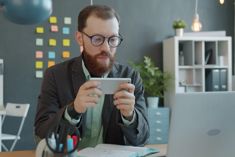 Smiling man playing a mobile game on his smartphone at a desk